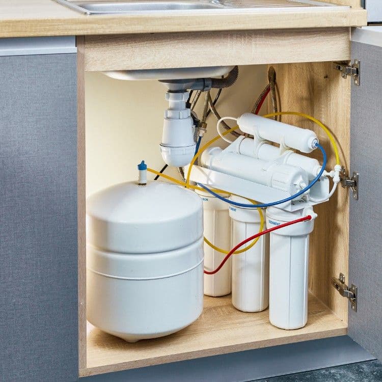 Under-sink water filtration system with tank and multiple filters installed in kitchen cabinet.