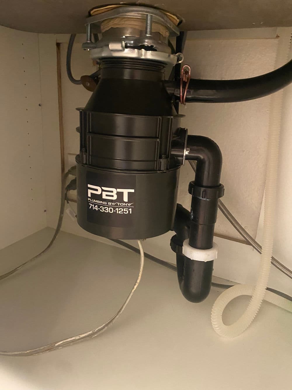 Black garbage disposal unit installed under kitchen sink with plumbing connections visible.