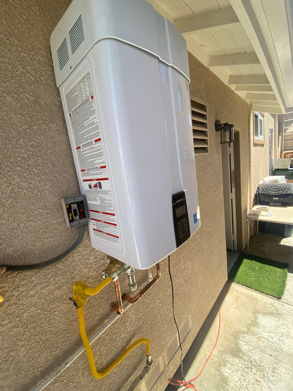 Tankless water heater installed on a wall with plumbing connections, near garage entrance.