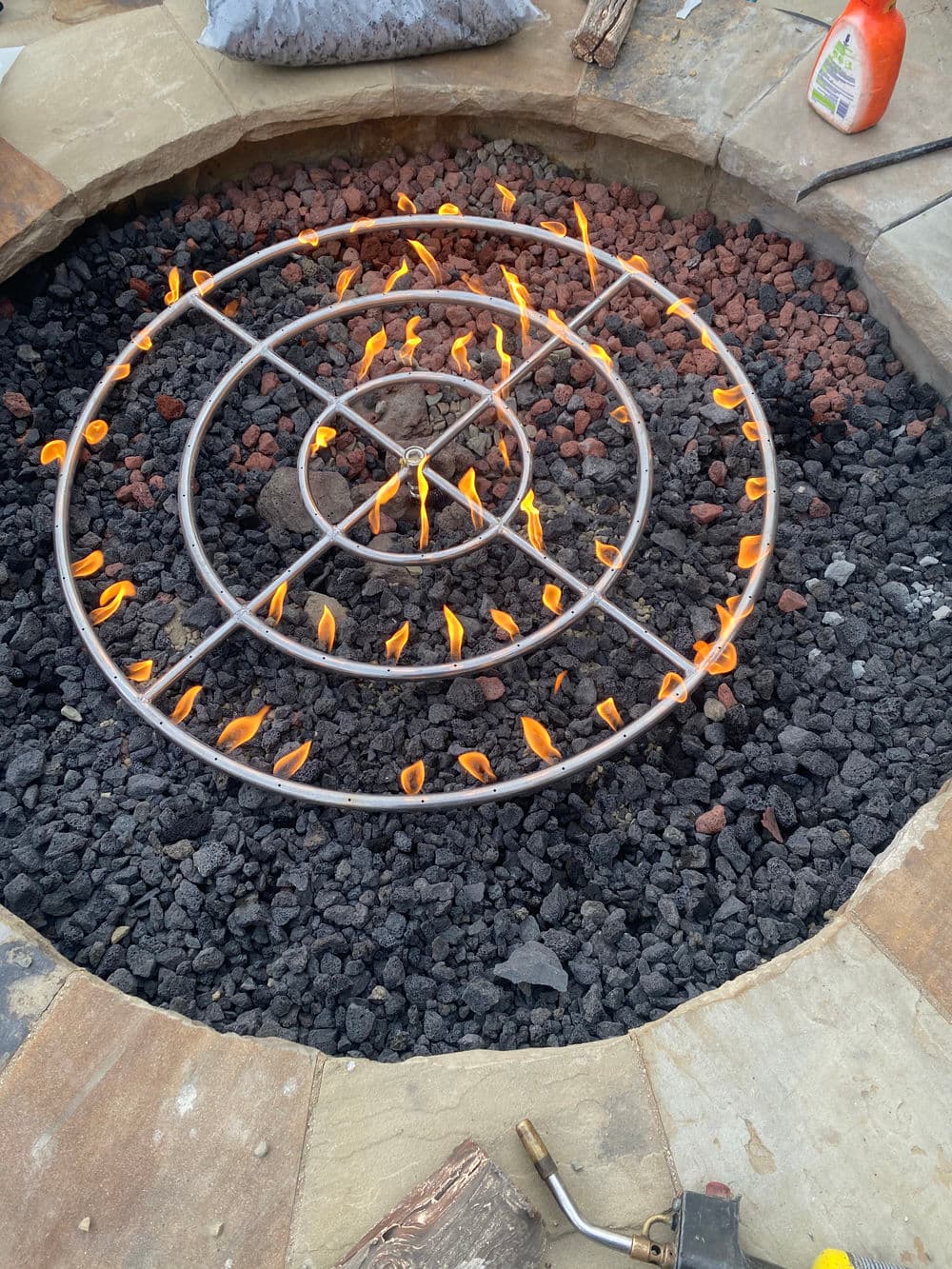 Fire pit with a circular grate surrounded by black lava rocks and flames. Outdoor relaxation.